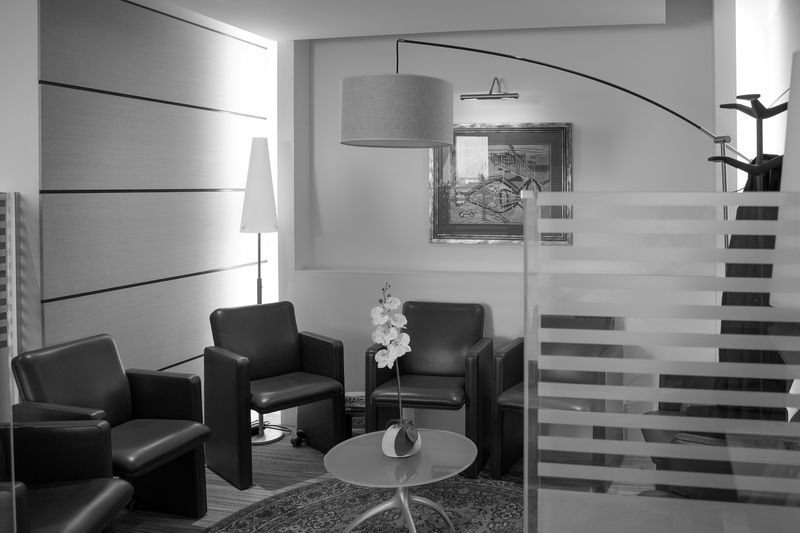 Salle d'attente du cabinet en noir et blanc : fauteuils, lampe à arc, cloisons vitrées